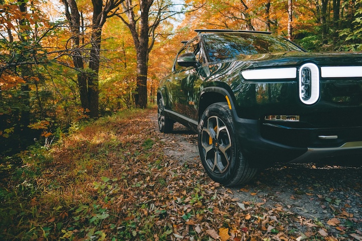 Rivian R1S parked in a forest with autumn leaves